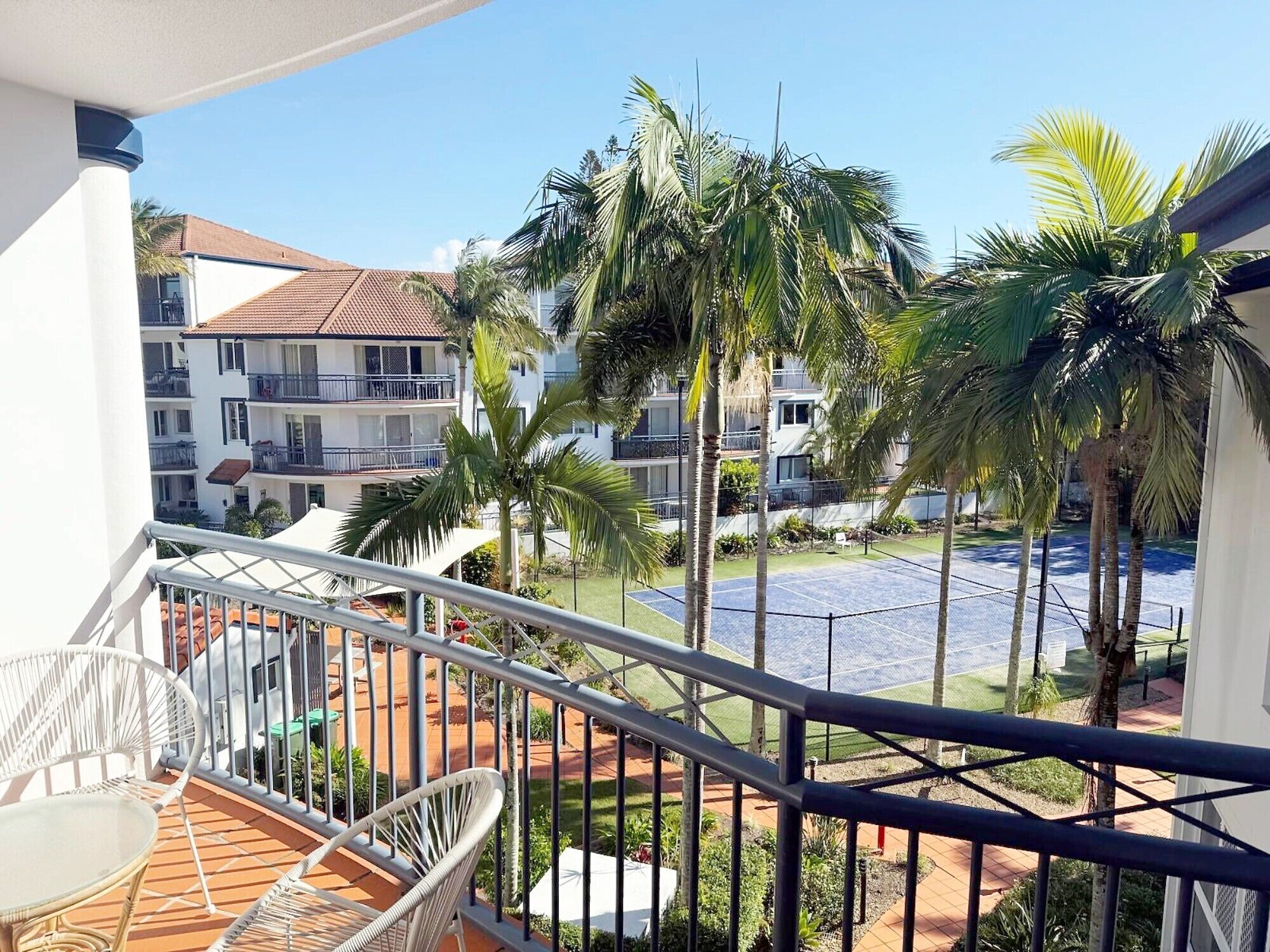Un balcón con vista a una piscina, palmeras y un edificio con balcones.
