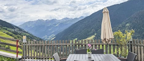 An outdoor seating area with a table and chairs, a wooden fence, and a mountain view.