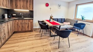 A modern kitchen with wooden cabinets, a dining table with chairs, and a red runner. There is a sofa and a window with a view.