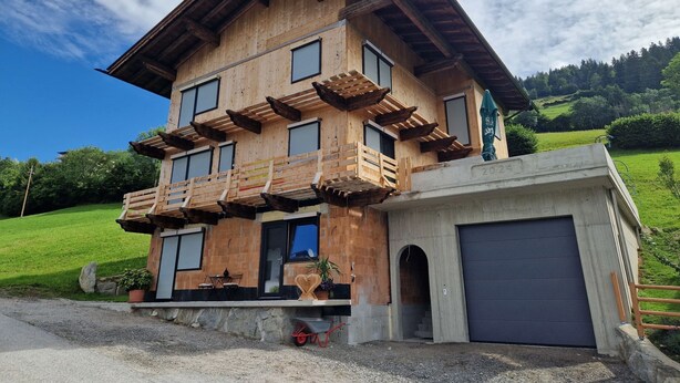 A multi-story wooden house with a balcony, a garage, and a well-maintained lawn.