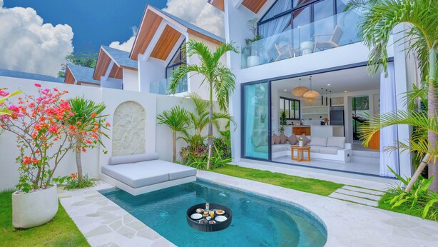 Una casa moderna con piscina, mobiliario exterior y exuberante vegetación.