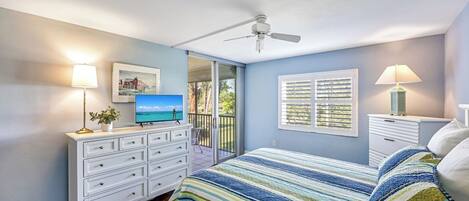Un dormitorio con cama, cómoda, televisor, ventilador de techo y ventana con persianas.