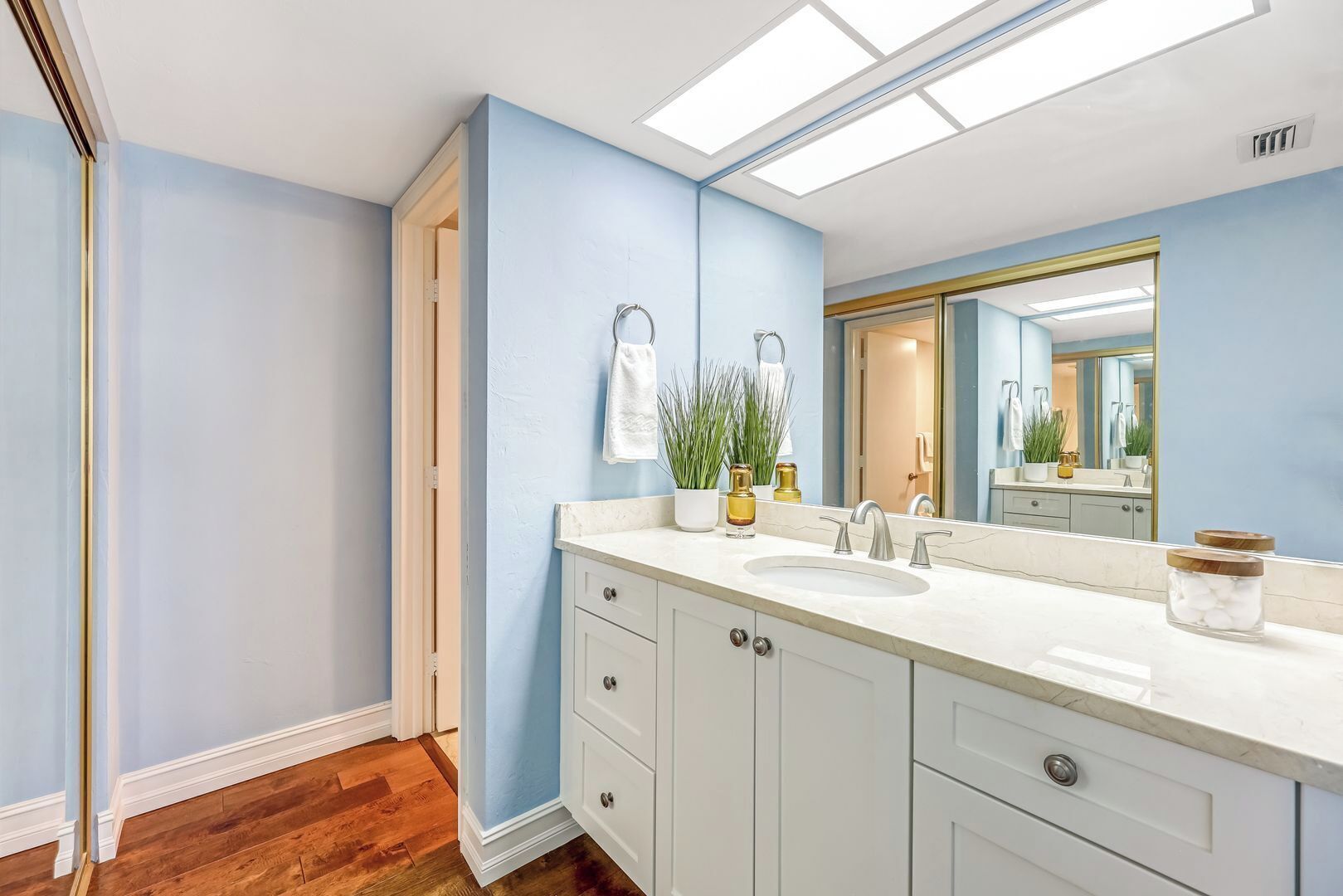 Een badkamer met een wit wastafelmeubel, een grote spiegel en een plafondlamp.