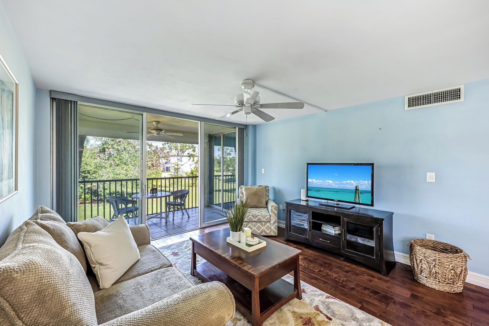 A living room with a sofa, coffee table, TV, and a balcony with outdoor furniture.