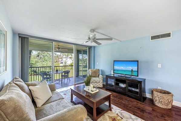 A living room with a sofa, coffee table, TV, and a balcony with outdoor furniture.