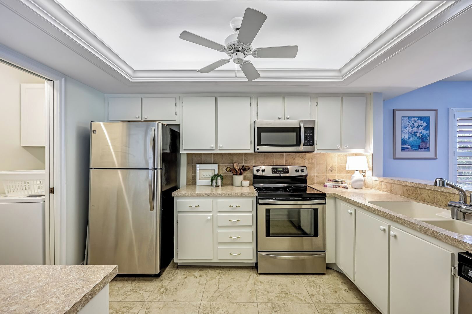A kitchen with white cabinets, stainless steel appliances, a ceiling fan, and a tiled backsplash.
