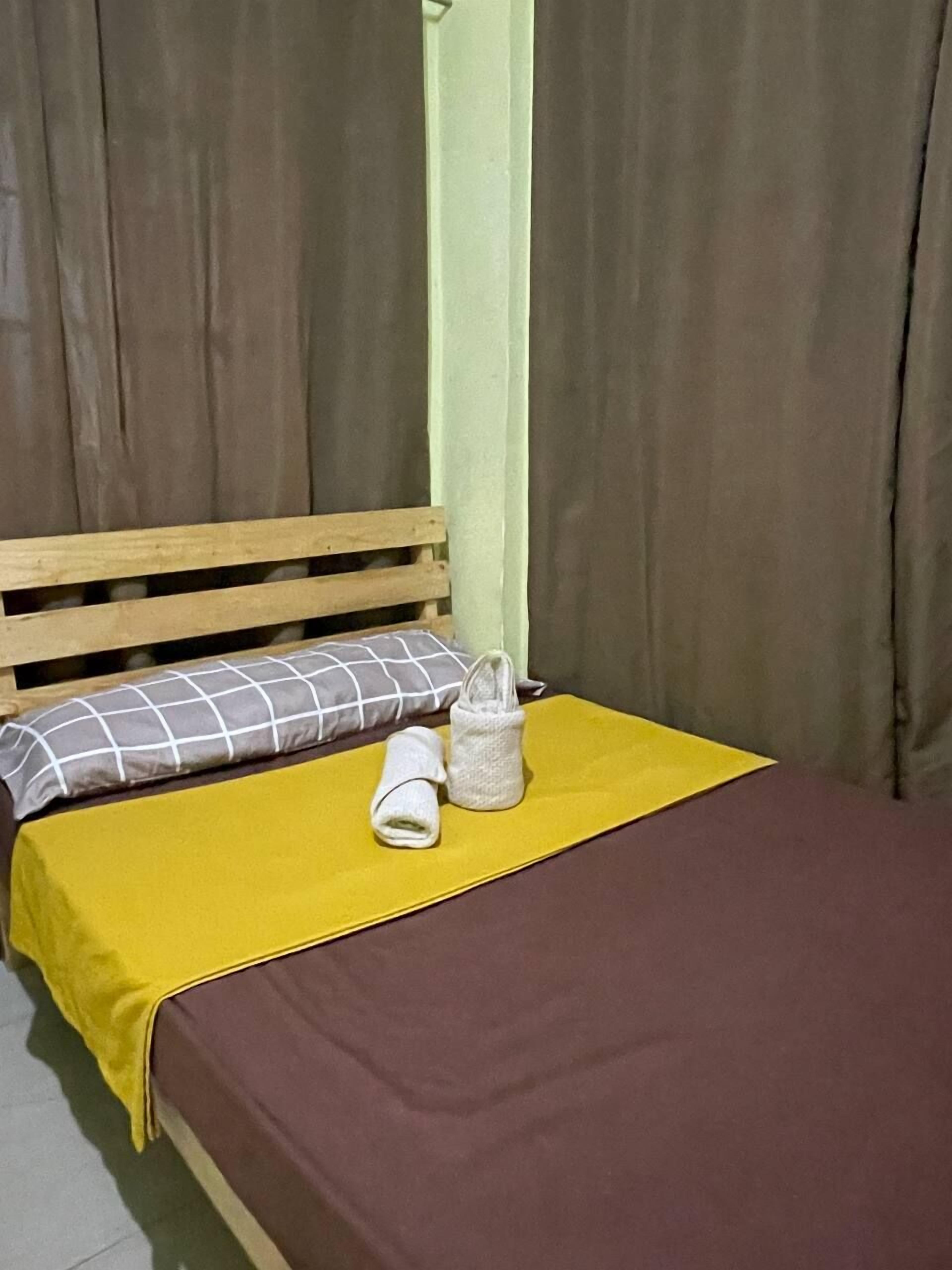 Una cama con colchón marrón, manta amarilla y almohada de estampado a cuadros.