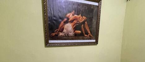 Quarto com uma pintura emoldurada de uma figura nua, uma mesa de metal branca e uma lixeira azul.