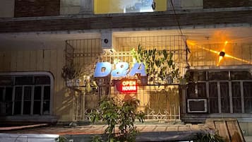 Una tienda D&A con un cartel que indica 'HORARIO DE ATENCIÓN', rodeada de plantas y una valla metálica.