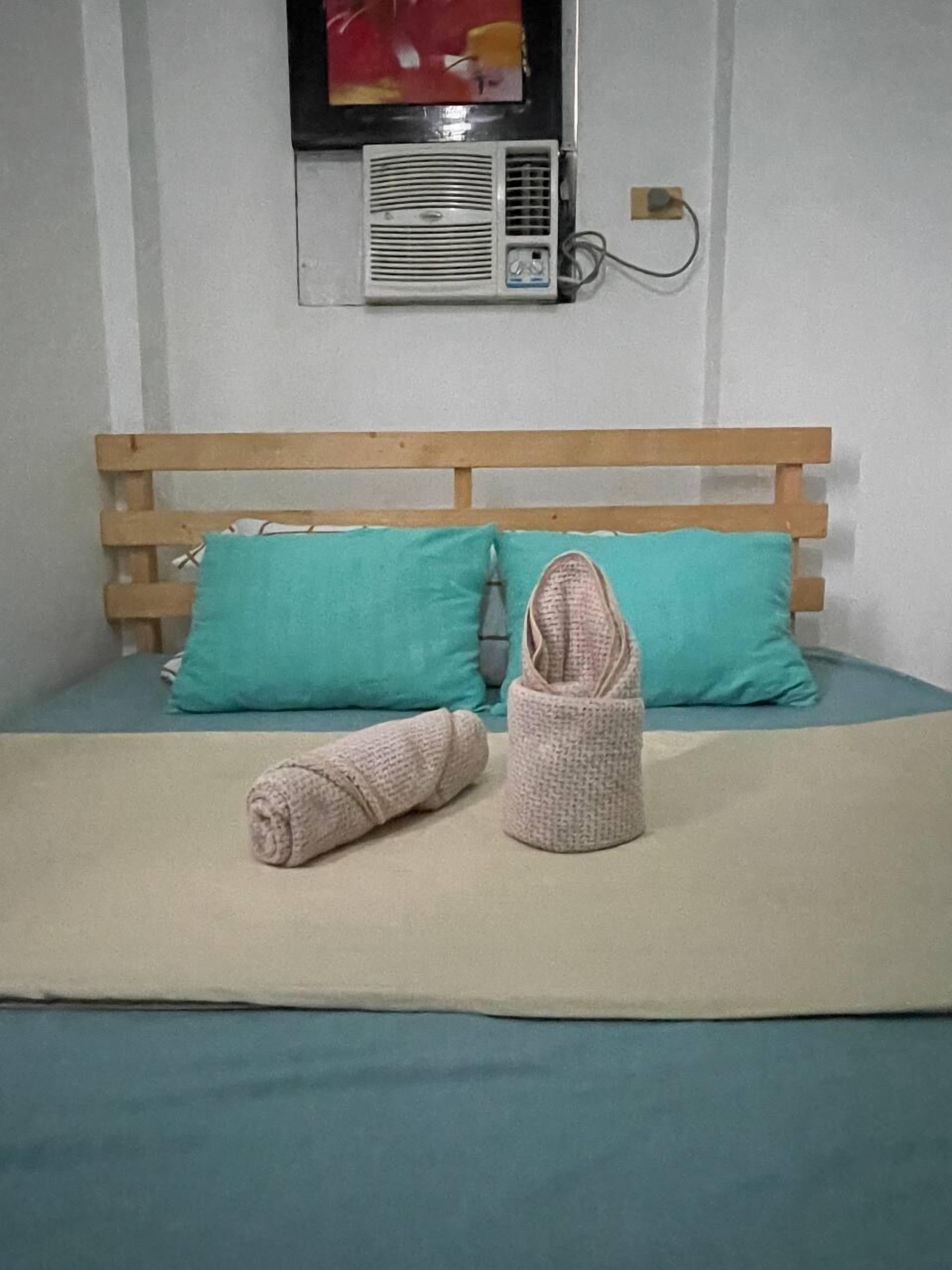 A bed with a wooden headboard, two teal pillows, and a beige blanket.