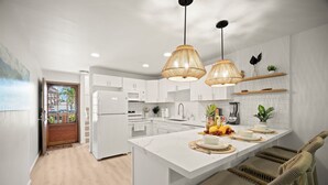 A modern kitchen with white cabinets, a central island, and wicker chairs. - BRAND NEW REMODELED 2/2 Family Getaway! Walk to Amazing Beach, AC & WiFi (Lihue)
