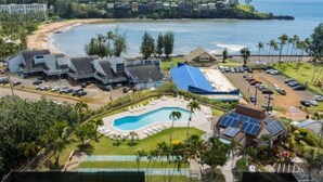 A tennis court with a pool, a beach, and a resort area with multiple buildings and parked cars. - BRAND NEW REMODELED 2/2 Family Getaway! Walk to Amazing Beach, AC & WiFi (Lihue)
