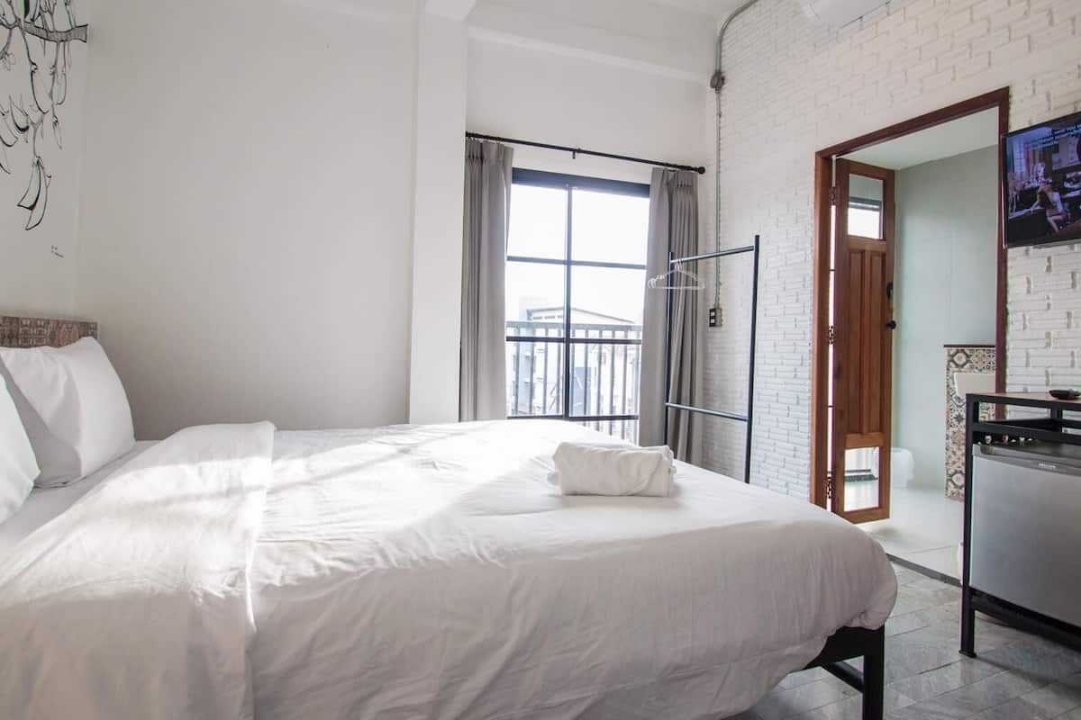 Habitación de hotel con una cama grande, un televisor montado en la pared y un balcón con vistas.