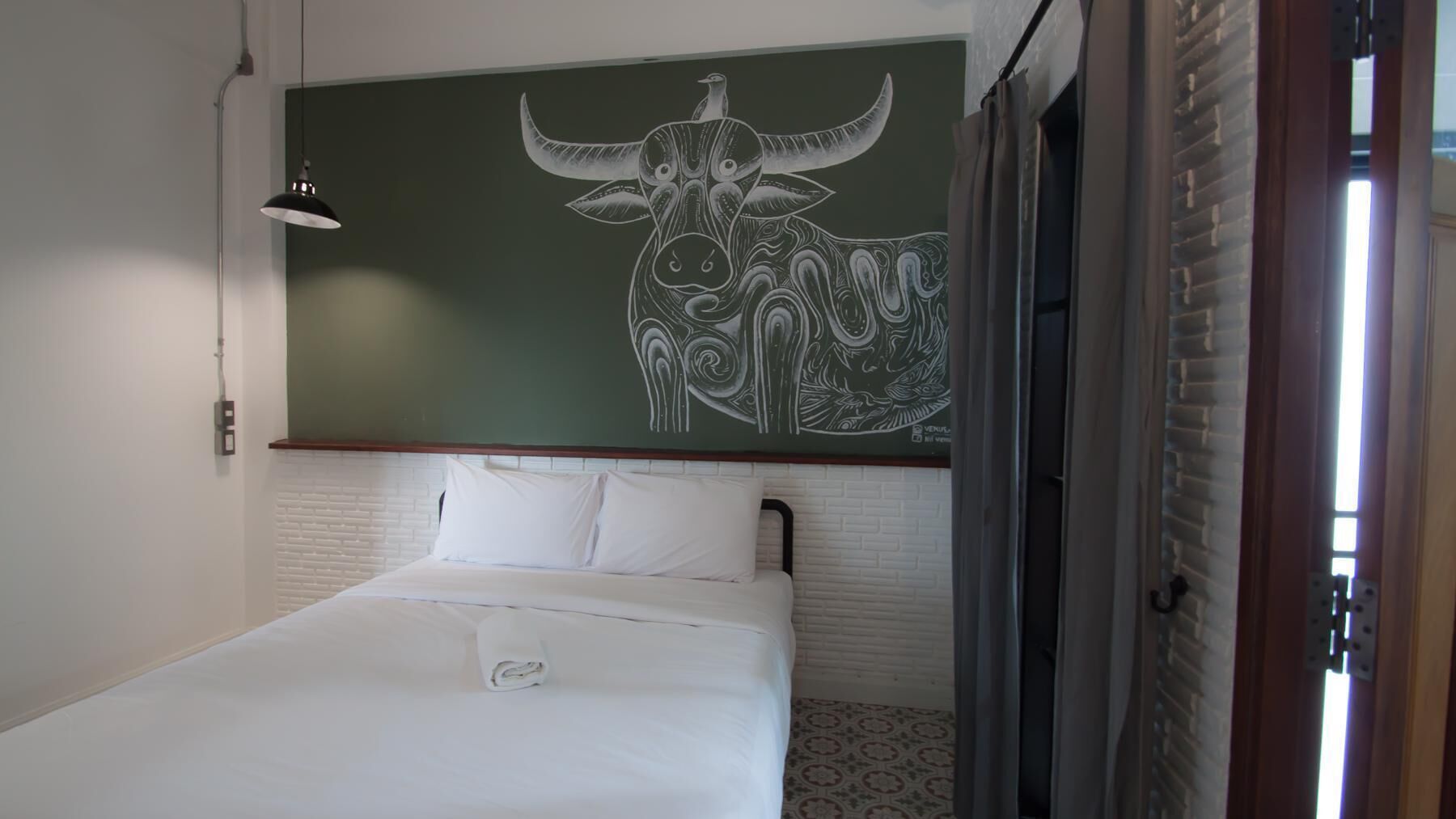 A hotel room with a bed, a wall-mounted artwork of a bull, a hanging lamp, and a patterned floor.