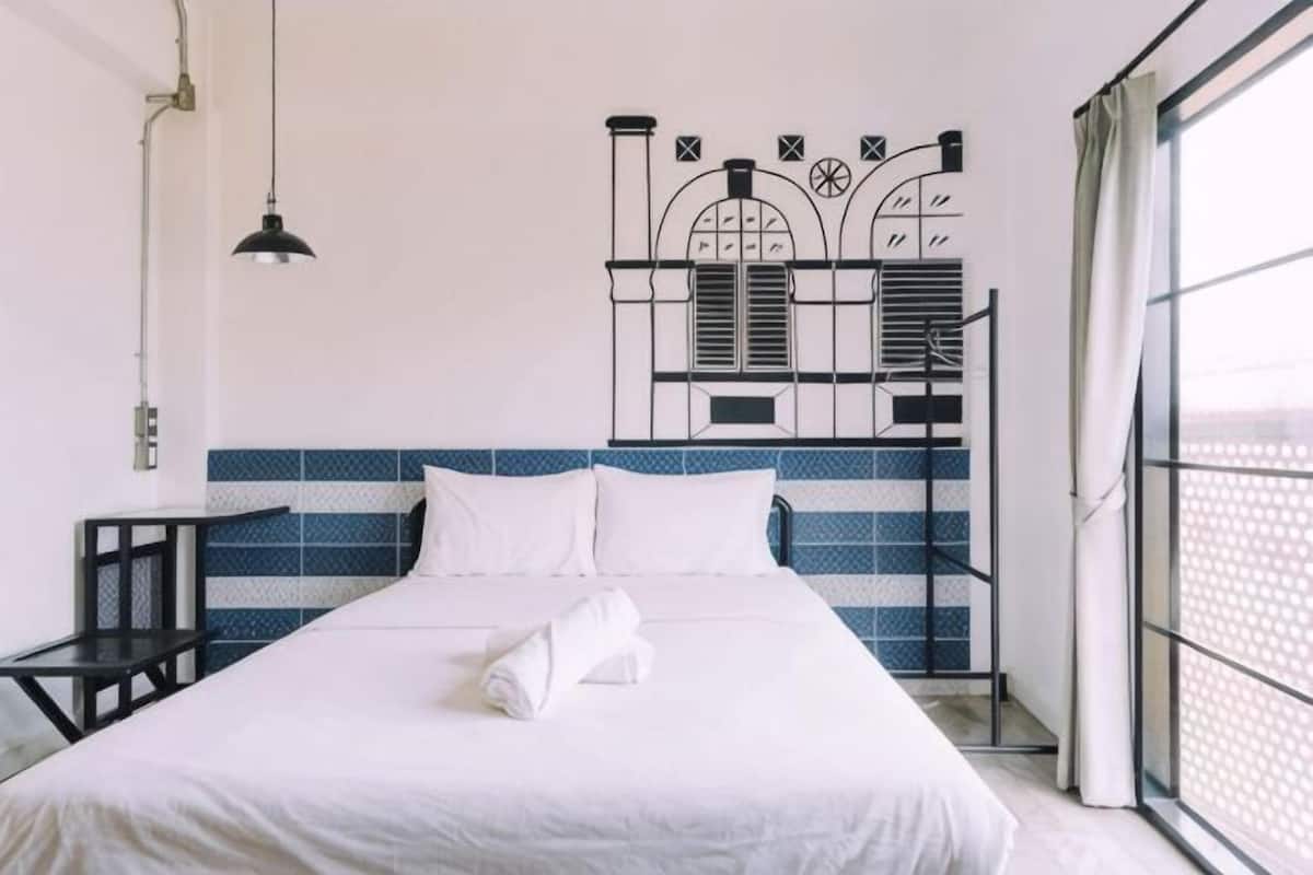 Una cama bien hecha con sábanas blancas, un cabecero de metal con un diseño decorativo, una mesita y un ventanal con vistas.