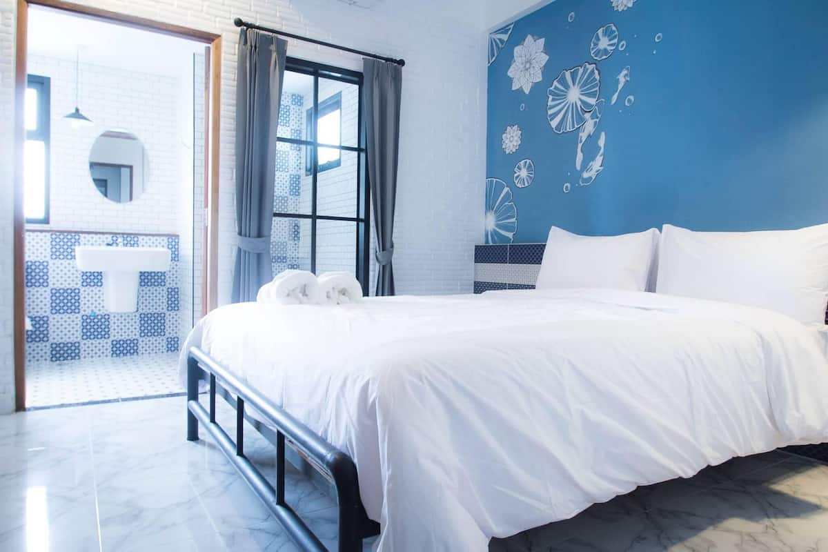 Un dormitorio con una cama grande, vistas al exterior y una pared azul con motivos florales.