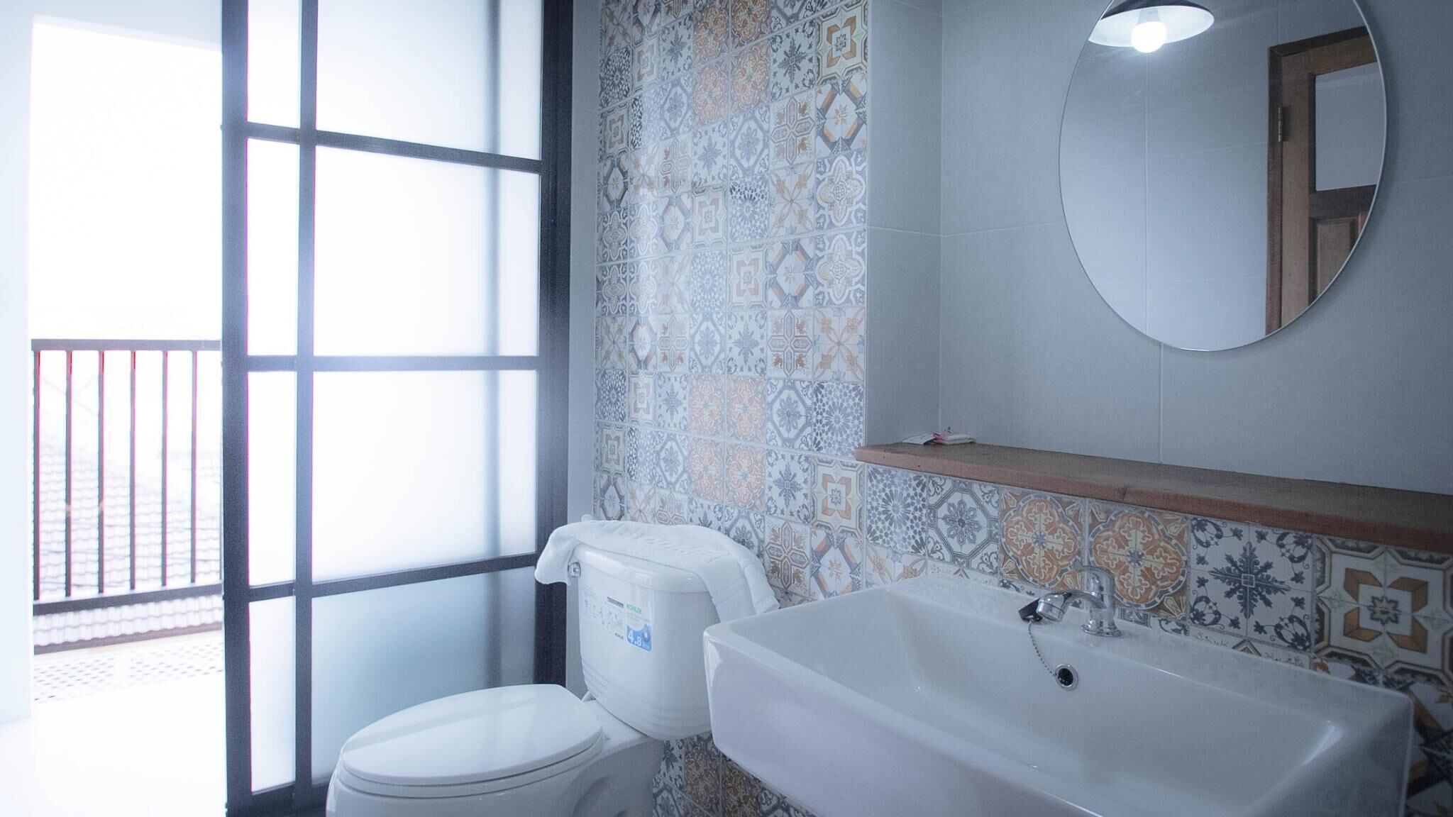 A bathroom with a toilet, a sink, and a mirror. There is a window with a view of a balcony.