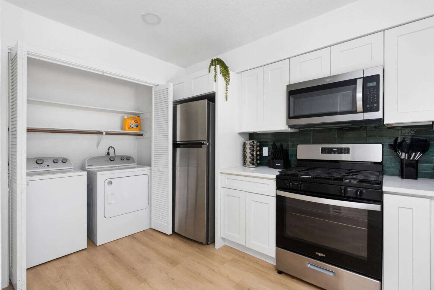 A modern kitchen with white cabinets, a stainless steel refrigerator, a microwave, a stove, and a dishwasher.