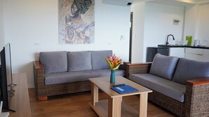 A living room with a grey sofa, a wooden coffee table with a vase of flowers, and a kitchen in the background. - Tablas Seaview Homestay (Ferrol)