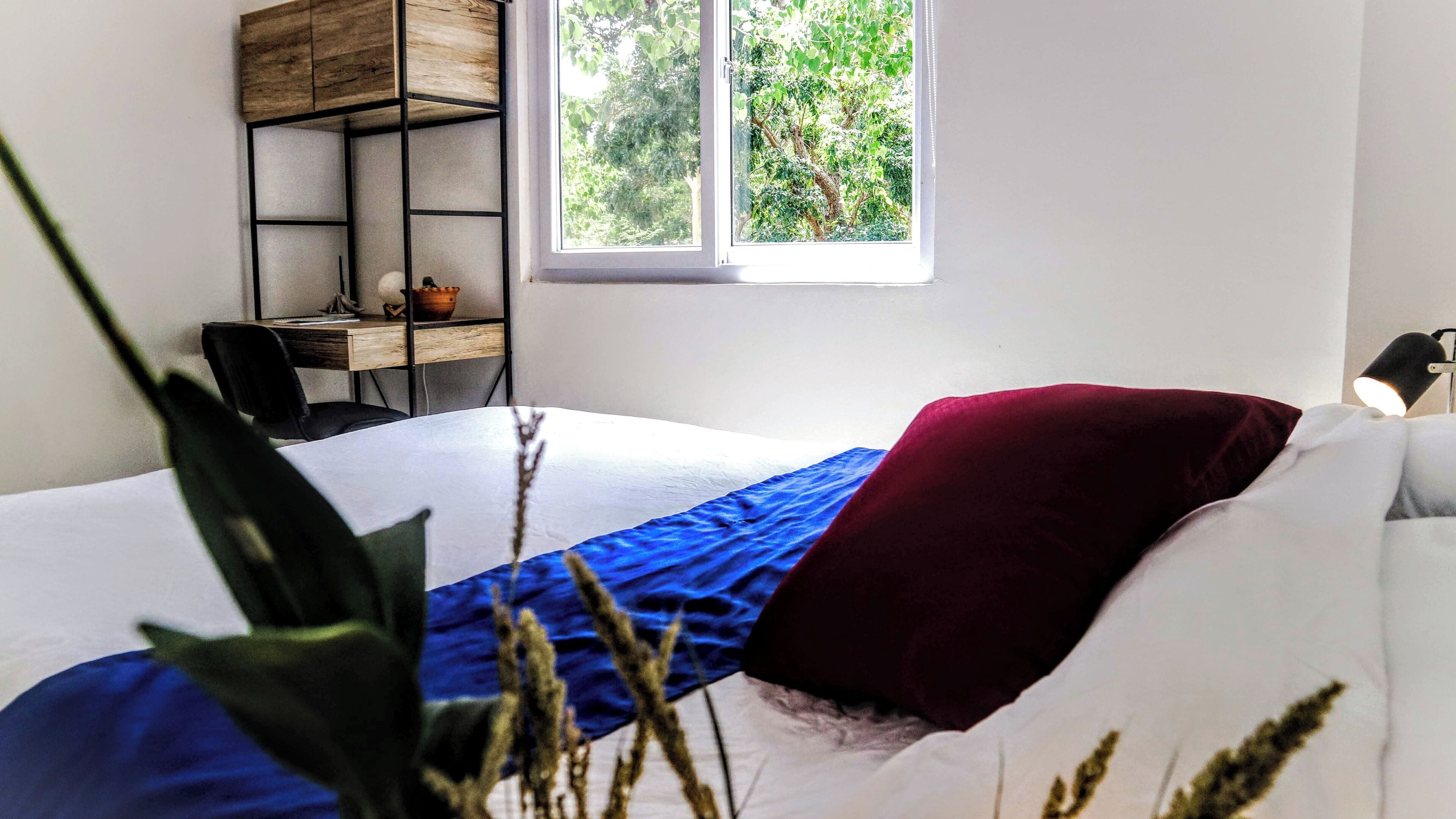 Un dormitorio con cama, escritorio y ventana con vista a la vegetación.