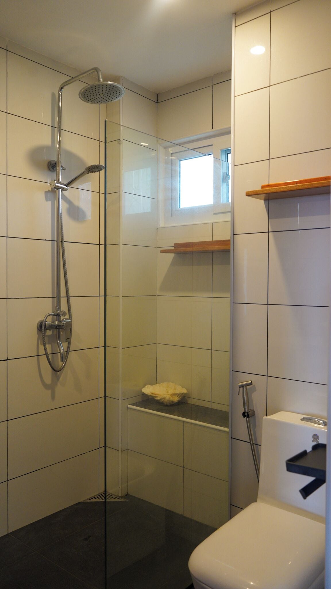 A bathroom with a glass-enclosed shower, a toilet, and a small window.