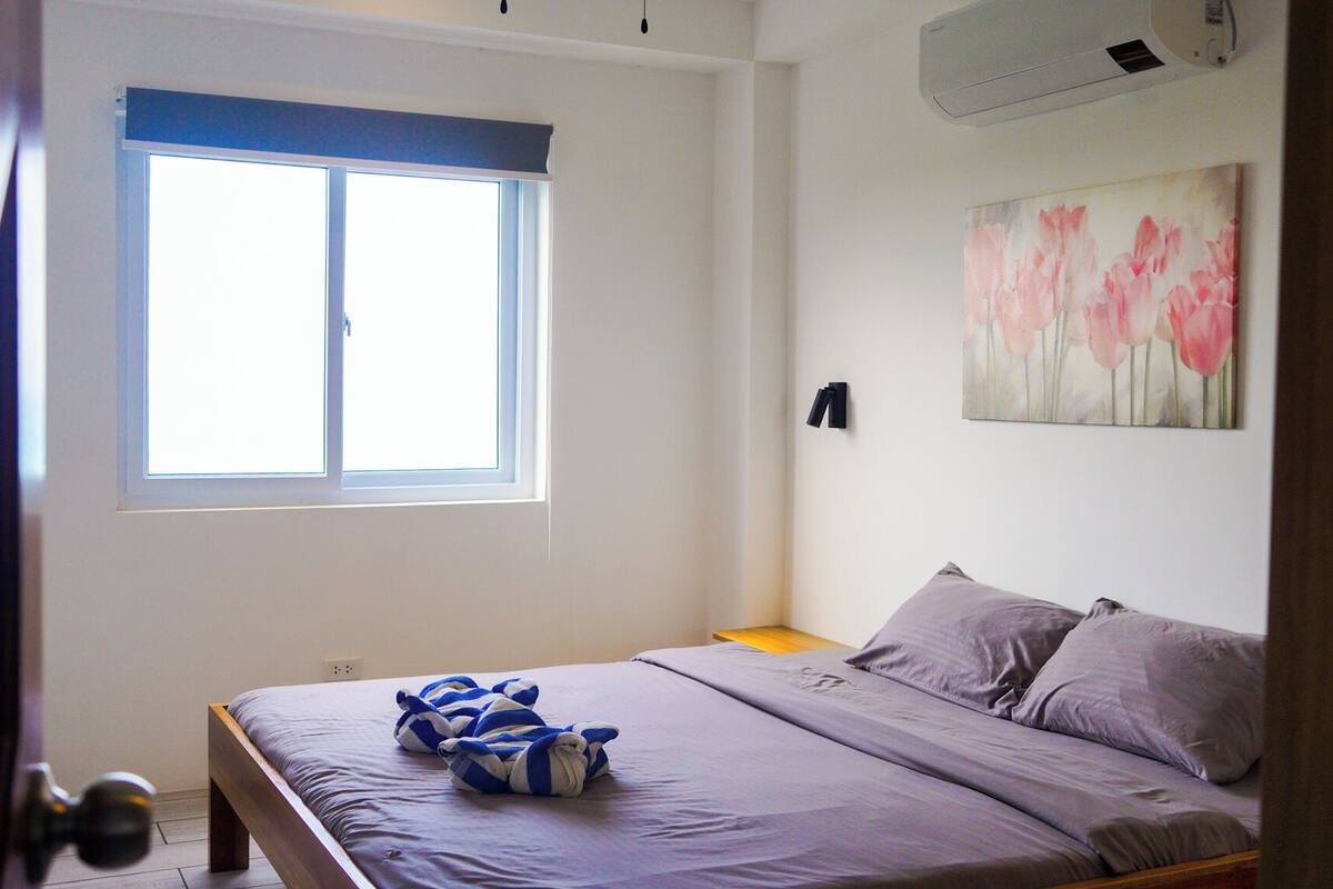 A bedroom with a bed, a window, and a painting on the wall.