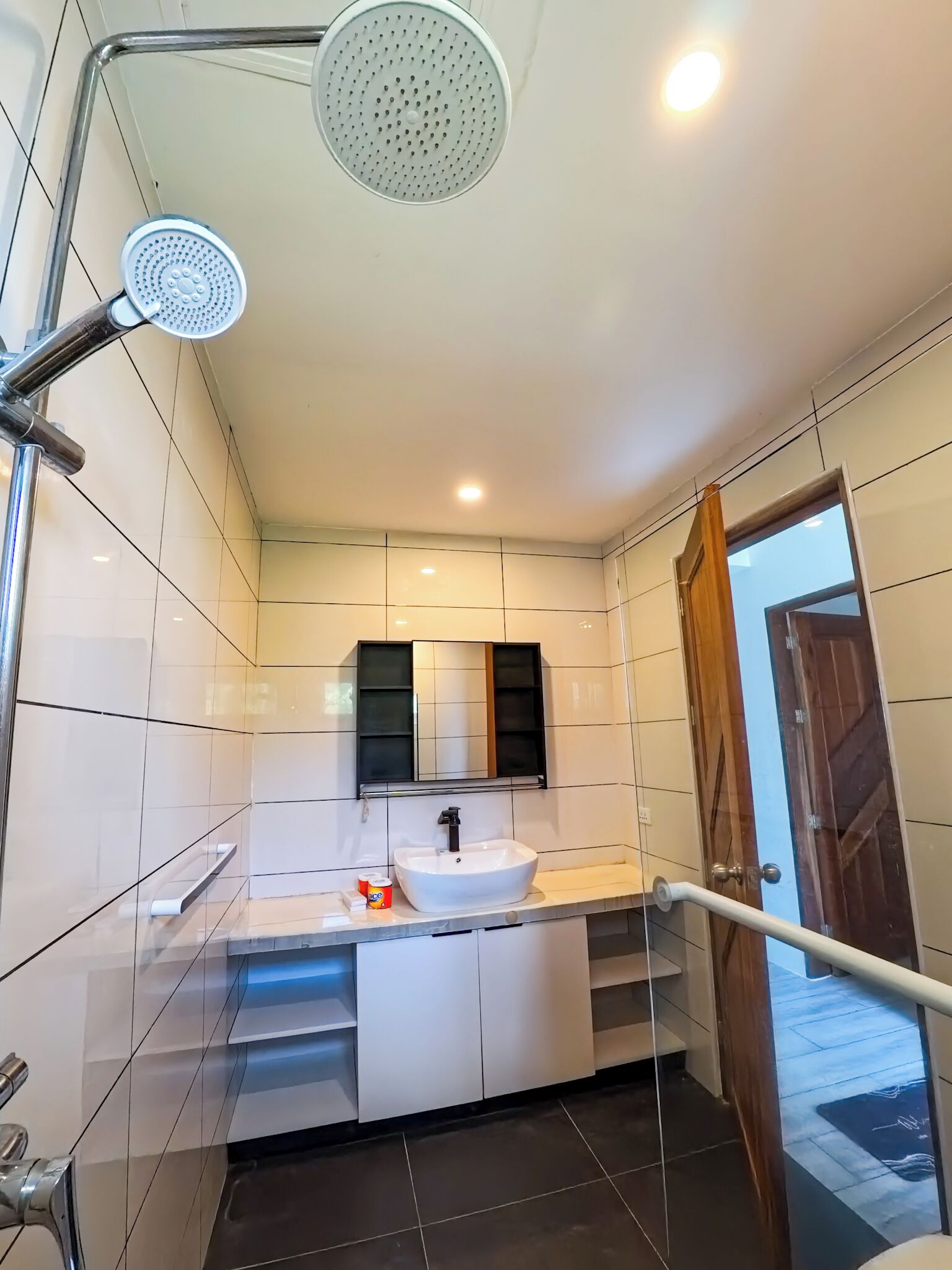 Un baño moderno con un lavamanos blanco, un espejo y una ducha con cabezal de ducha manual.