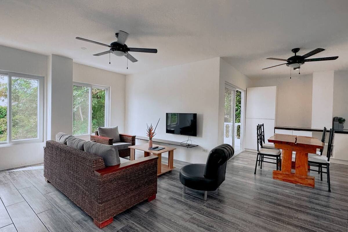 A modern living room with a sofa, a dining table, and two ceiling fans.