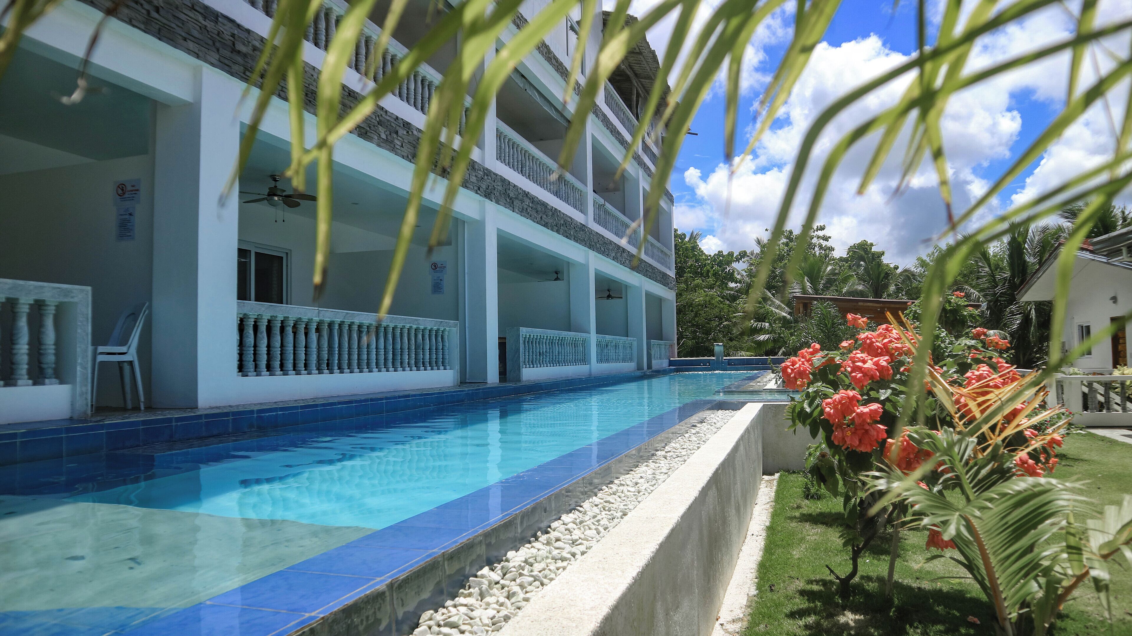 Un hotel con piscina, varios balcones y un jardín lleno de flores.