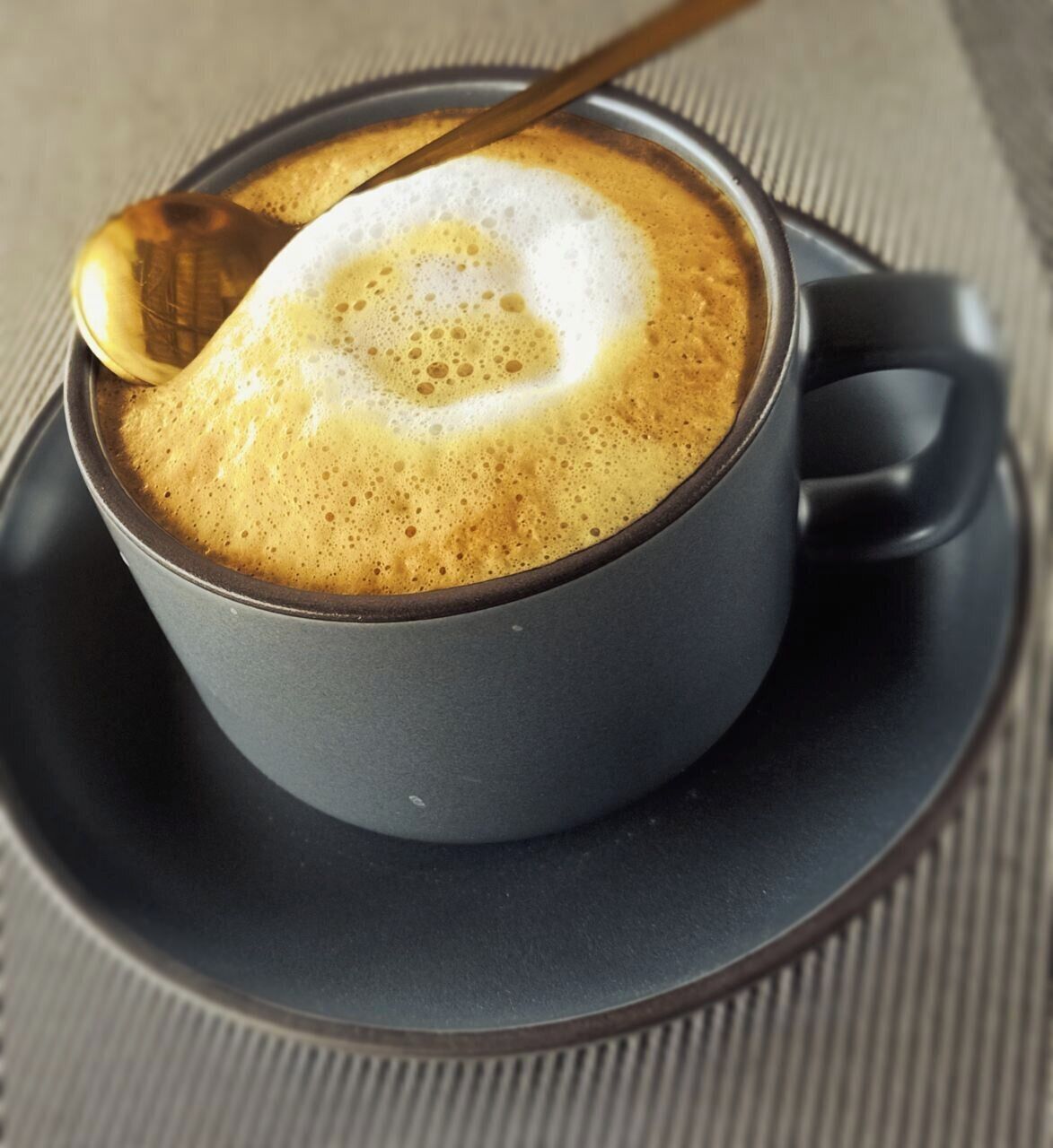 A cup of coffee with a spoon, on a saucer.