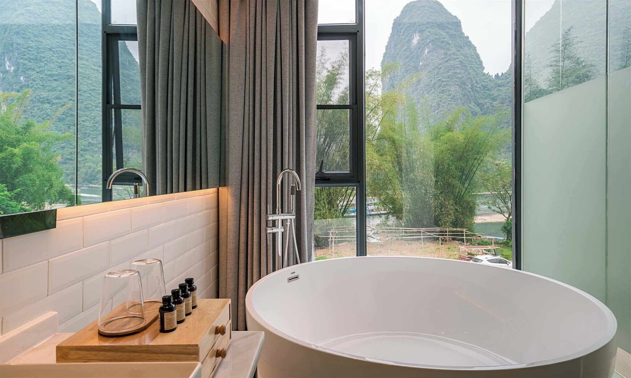 Un baño moderno con una bañera independiente, un mueble de tocador de madera con espejo y vistas a un paisaje montañoso a través de amplios ventanales.