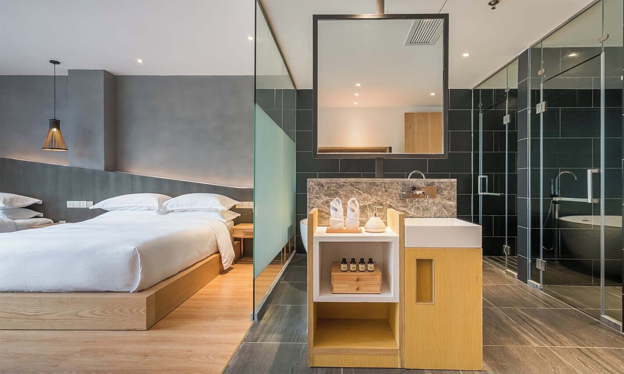 Ein modernes Hotelzimmer mit Bett, Schminktisch mit Spiegel und Duschbereich.
