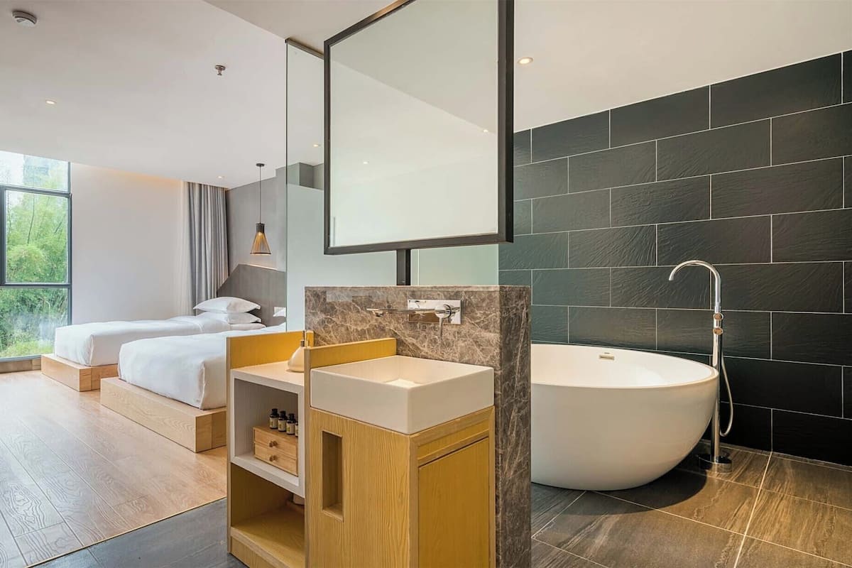 Una habitación de hotel moderna con un ventanal grande, una bañera y un tocador de madera.