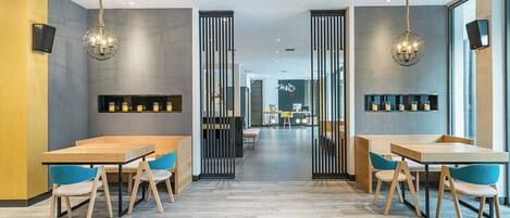 A modern restaurant with wooden tables and chairs, pendant lights, and a central divider.