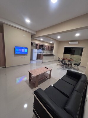 A modern living room with a black leather sofa, a wooden coffee table, and a flat-screen TV mounted on the wall. - MEDIEVAL DEPARTMENT (Luque)