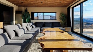 A modern living room with a wooden ceiling, a large sofa, a coffee table, and large windows offering a view of the outdoors. - Sauna BBQ with a spectacular view of Mt. Fuji｜Max 20 people｜The No. 10 Mt. (minamitsuru-gun yamanaka-ko hirano)