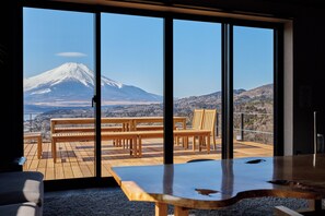 Ein Zimmer mit großen Fenstern und Blick auf einen Berg. Darin befindet sich ein Holztisch mit Bänken.