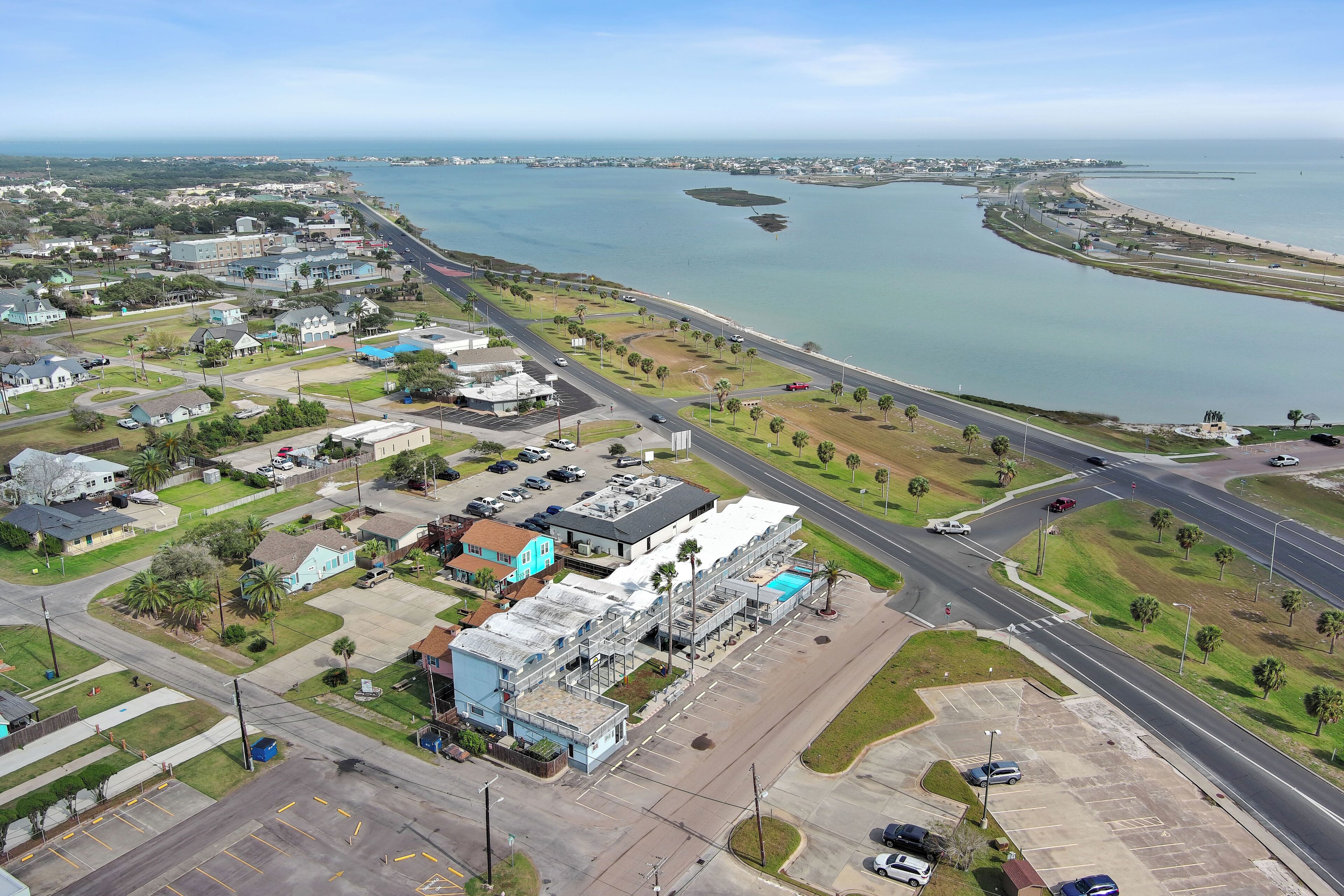 Vista aérea de una zona costera con un estacionamiento, edificios y una carretera que conduce a la playa.