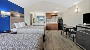 Ein Hotelzimmer mit zwei Betten, einer Küchenzeile, einem Essbereich und einem durch eine offene Tür einsehbaren Badezimmer.