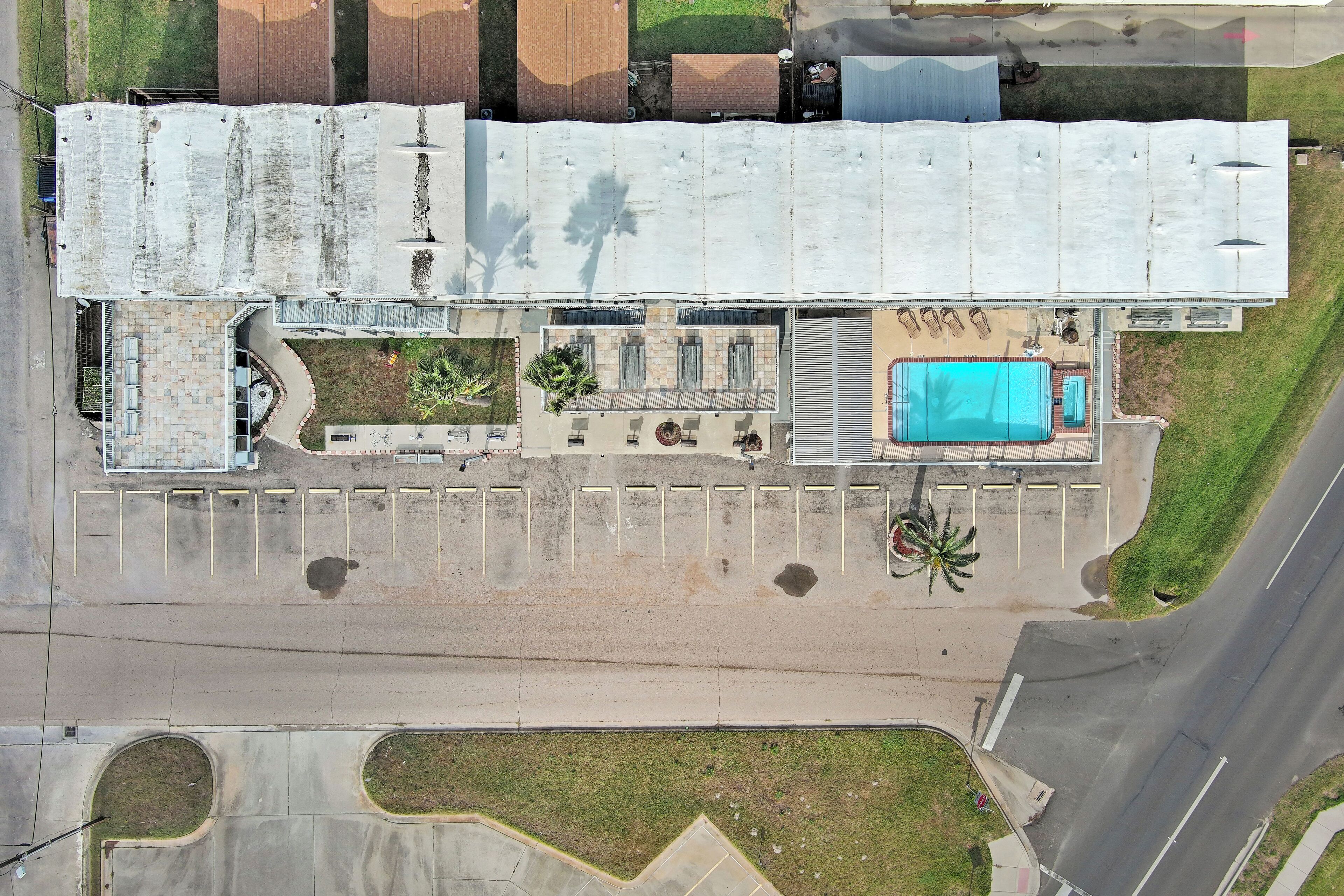 An aerial view of a hotel with a swimming pool, parking area, and a covered outdoor seating area.