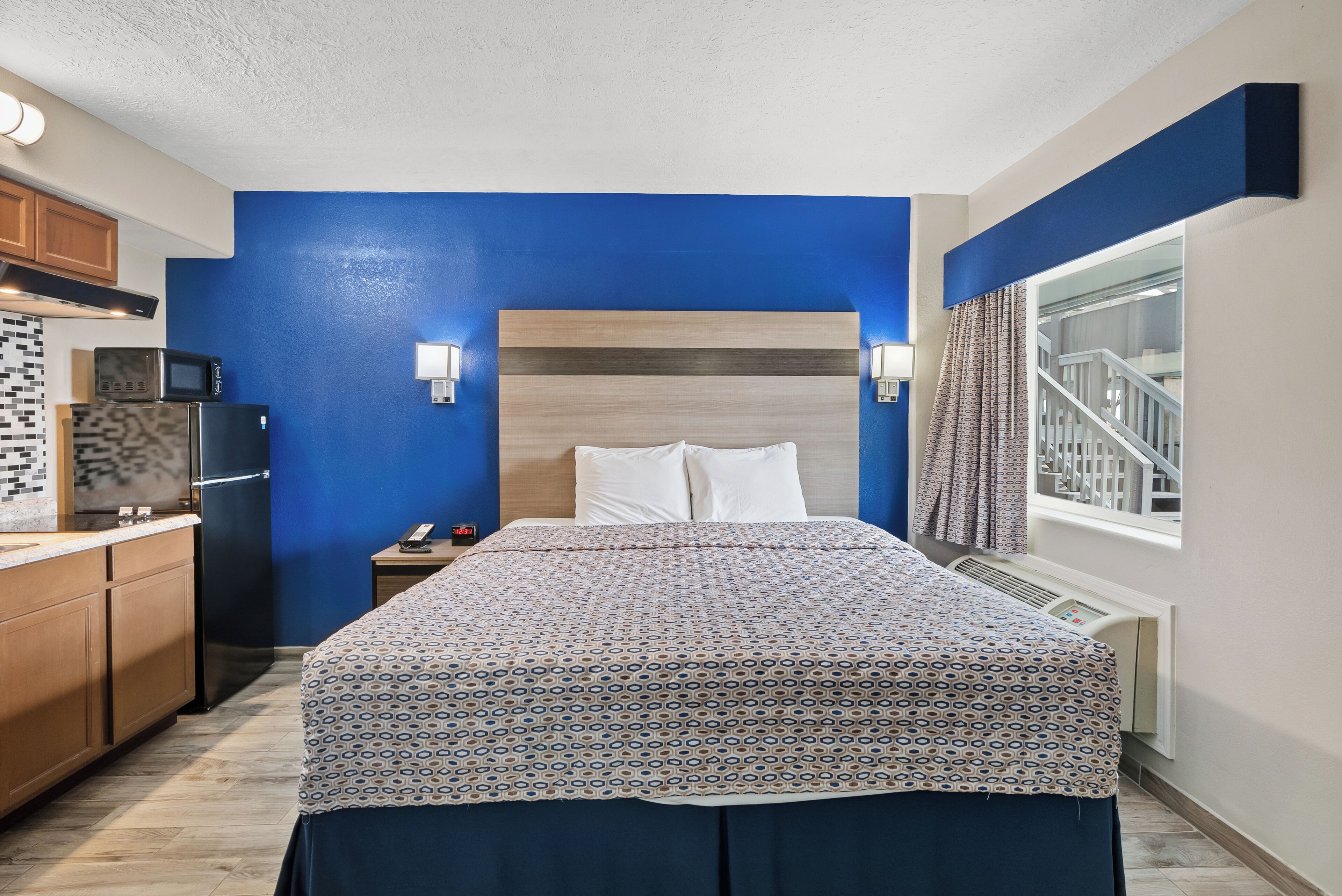 Habitación de hotel con cama, mesita de noche, microondas, refrigerador y ventana con vista a una escalera.