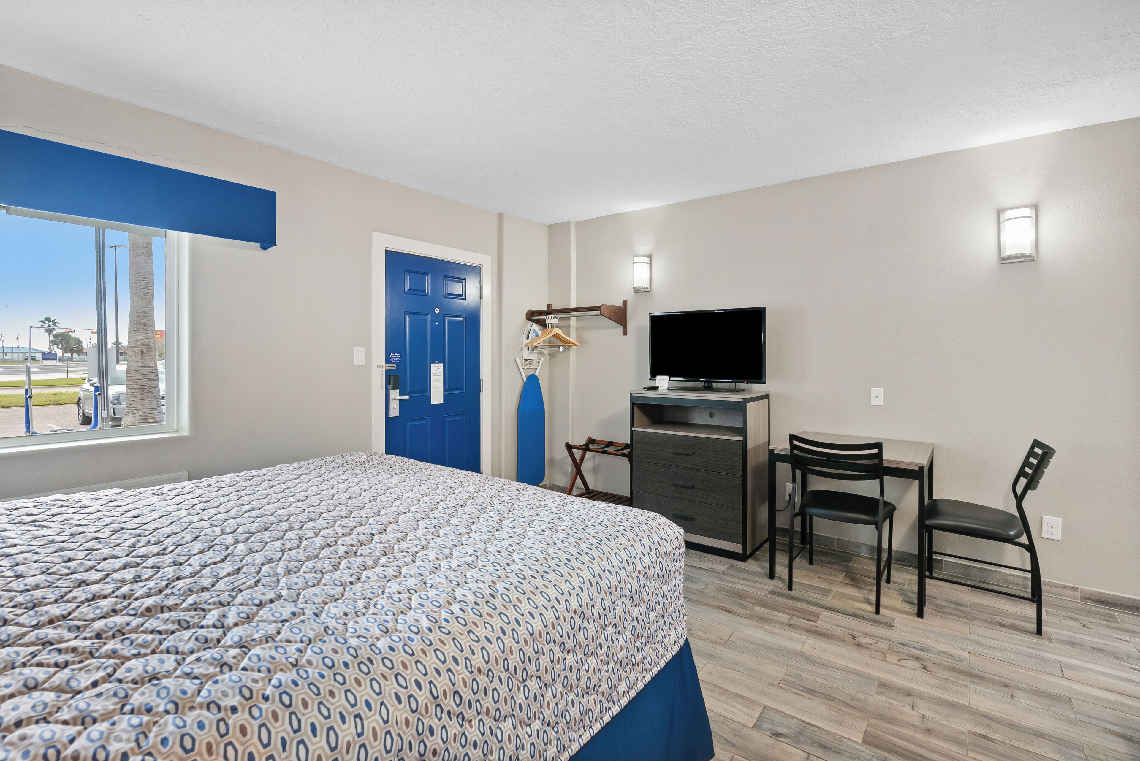 Una habitación de hotel con cama, escritorio, silla, televisor y puerta.