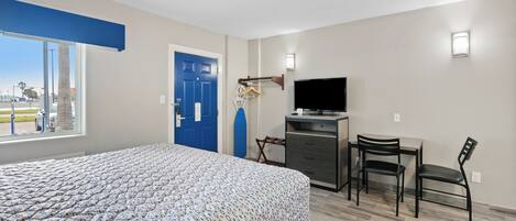 Una habitación de hotel con cama, escritorio, silla, televisor y puerta.
