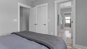 A bedroom with a bed, two white doors, and a hallway leading to a bathroom.