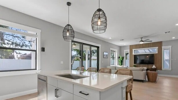A modern kitchen with a large island, pendant lighting, and a view to the outdoors.