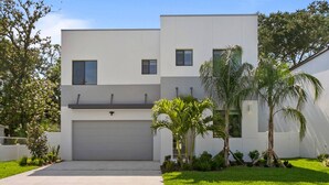 A modern two-story house with a garage, surrounded by a well-maintained lawn and palm trees.