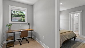 A bedroom with a bed, a desk with a chair, a window, and a door leading to another room.