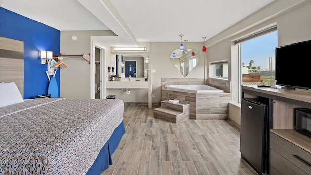 A hotel room with a bed, a bathroom with a bathtub, a sink, and a TV. - Waterview King Suite • Pool front, ground level (Rockport)