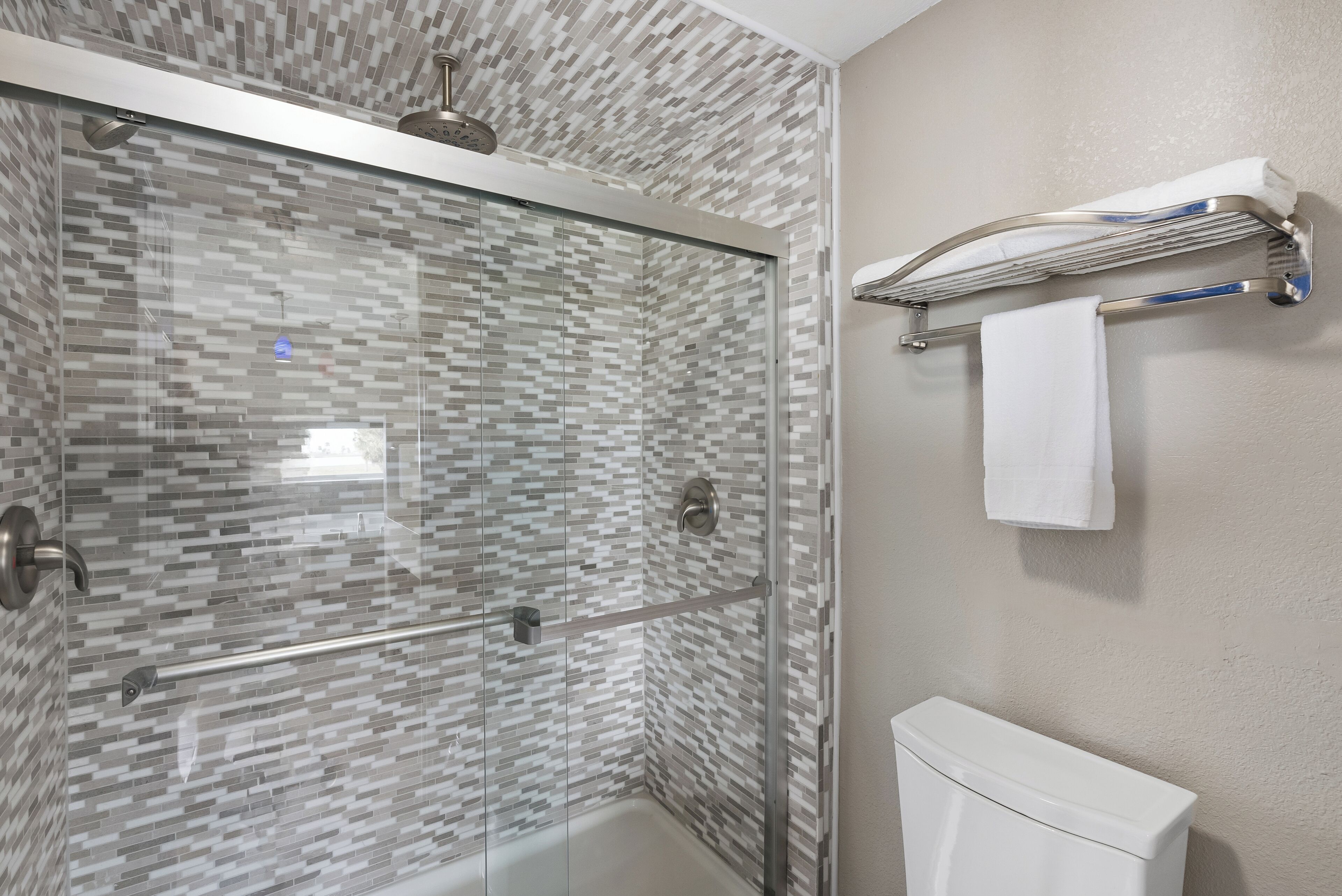 Un baño moderno con ducha de vidrio, inodoro blanco y perchero para toallas.