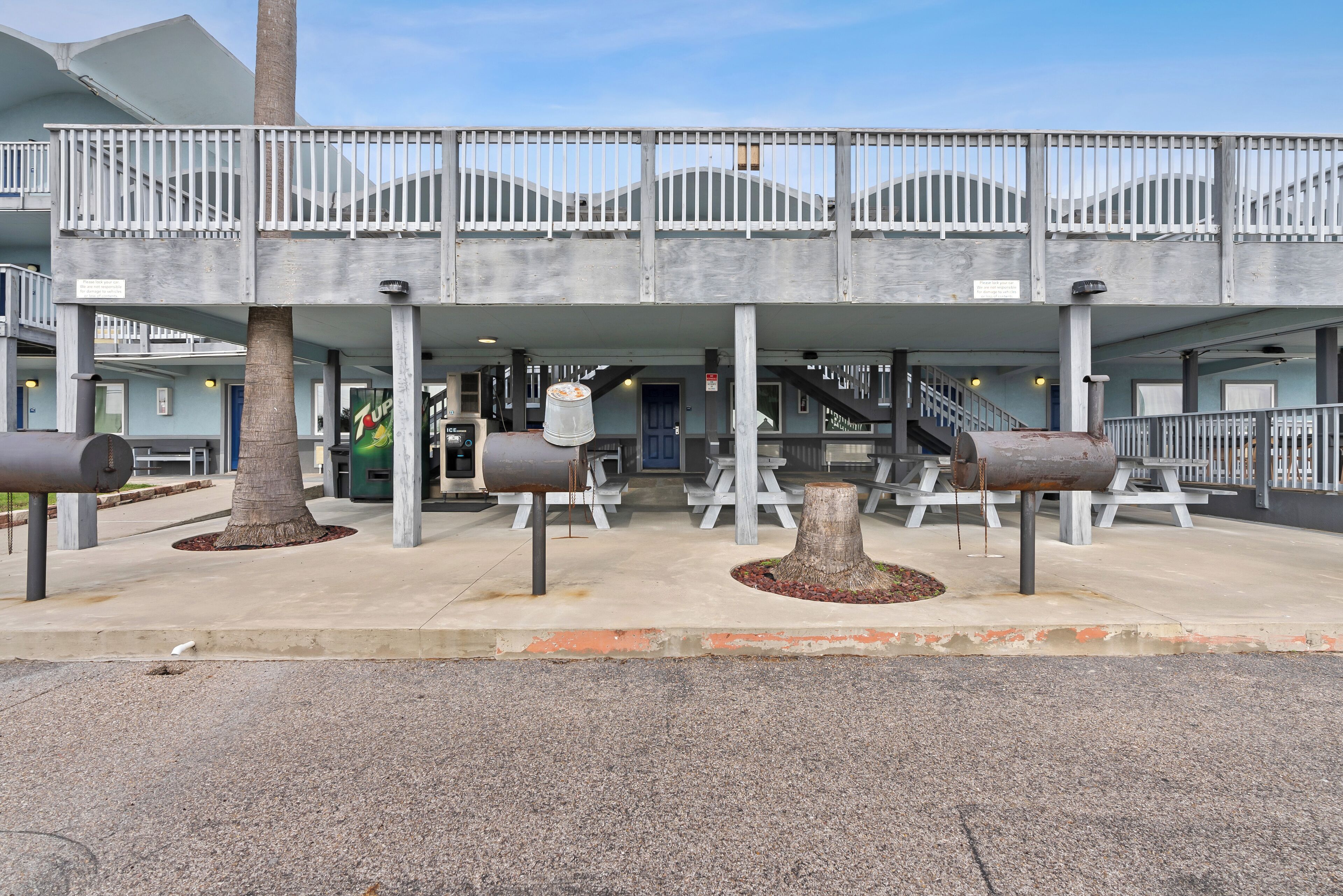 A building with a covered outdoor area, multiple trash bins, and a staircase leading to an upper level.